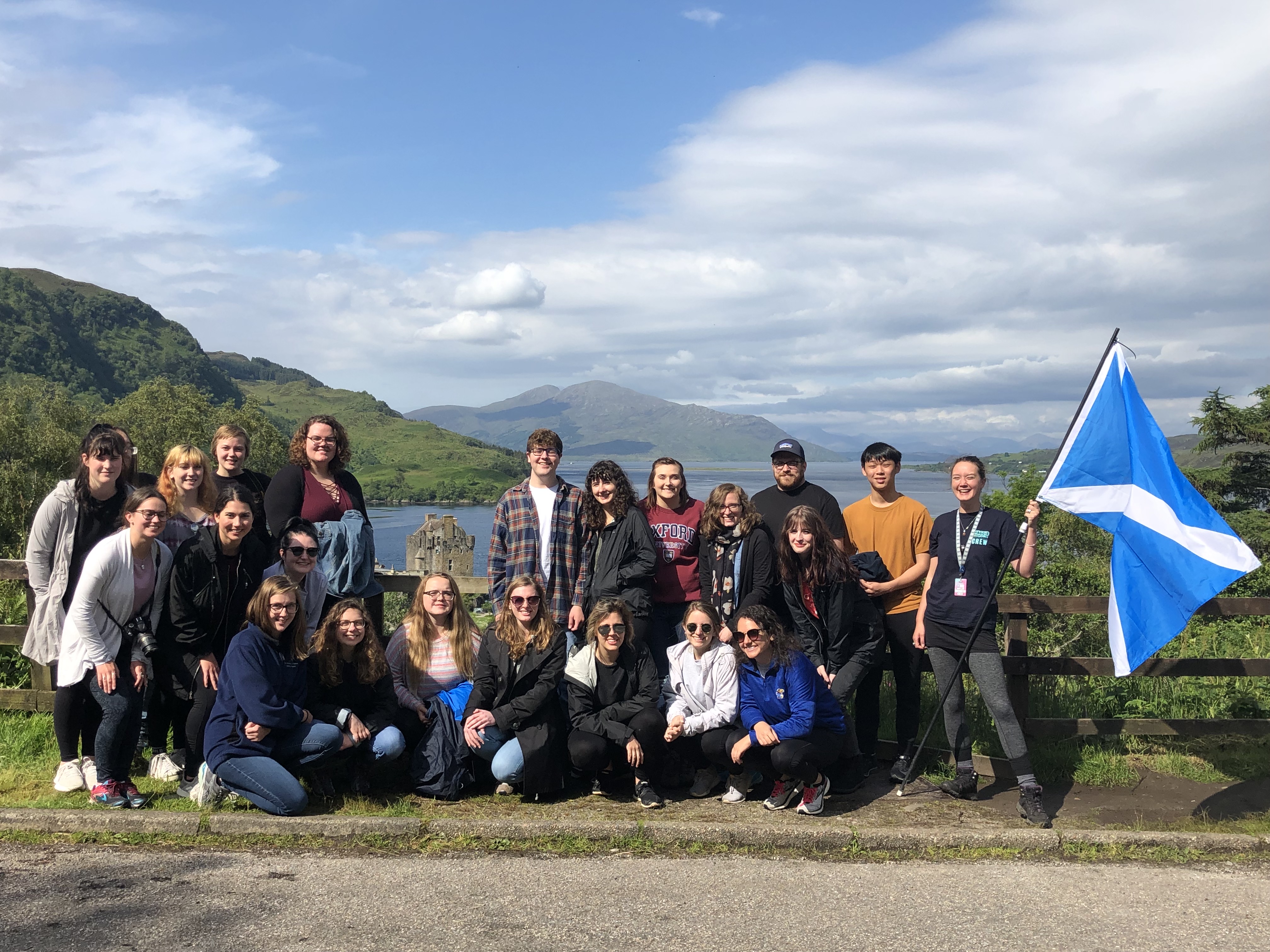 Group of 22 students and advisors stand together in front of lake in England