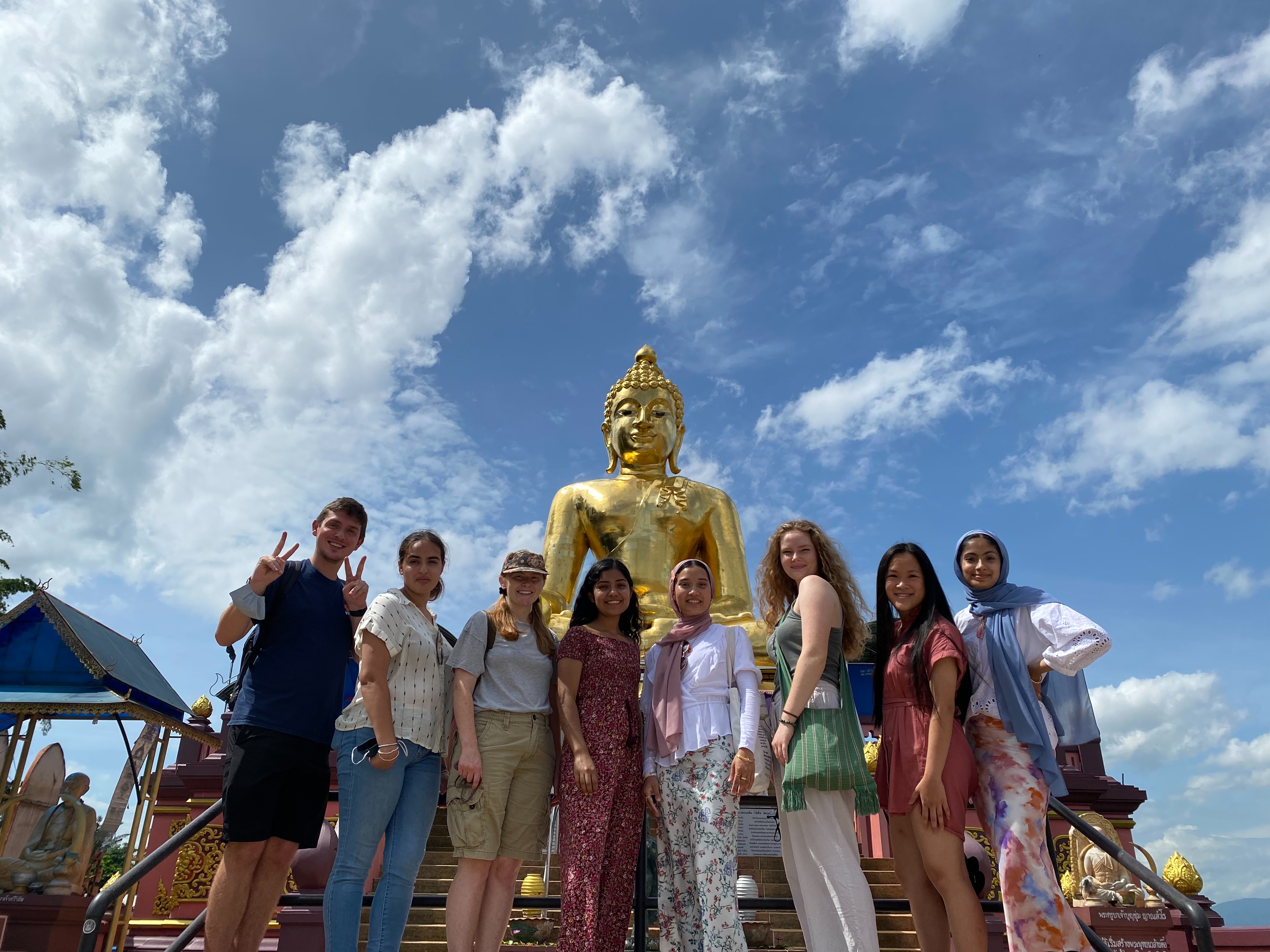 Eight students stand together in front of golden statue in Thailand