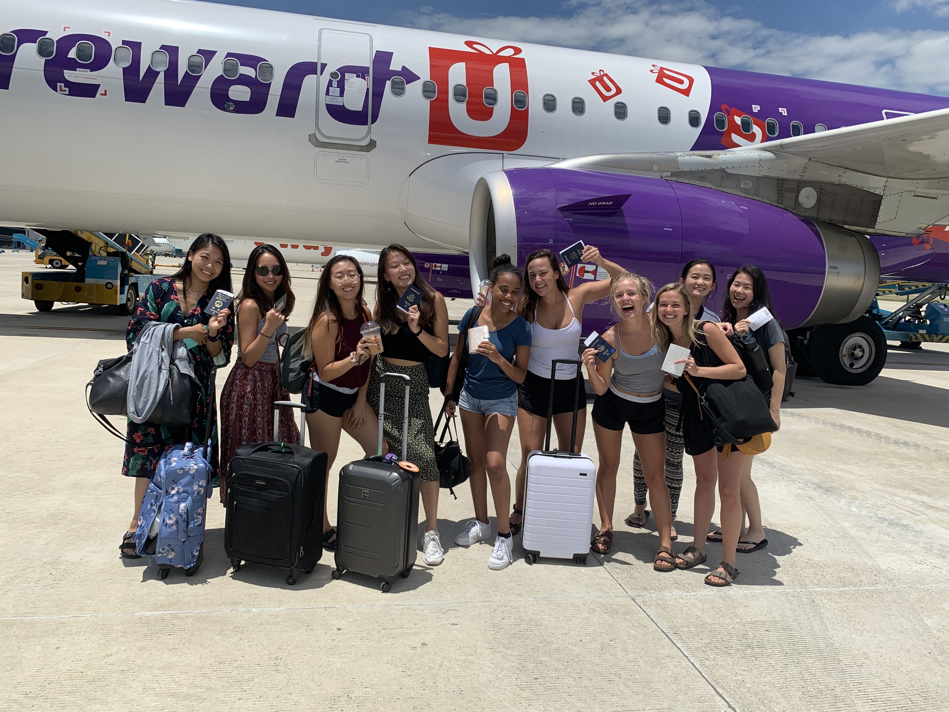 Ten students hold their passports in front of plane on the tarmac